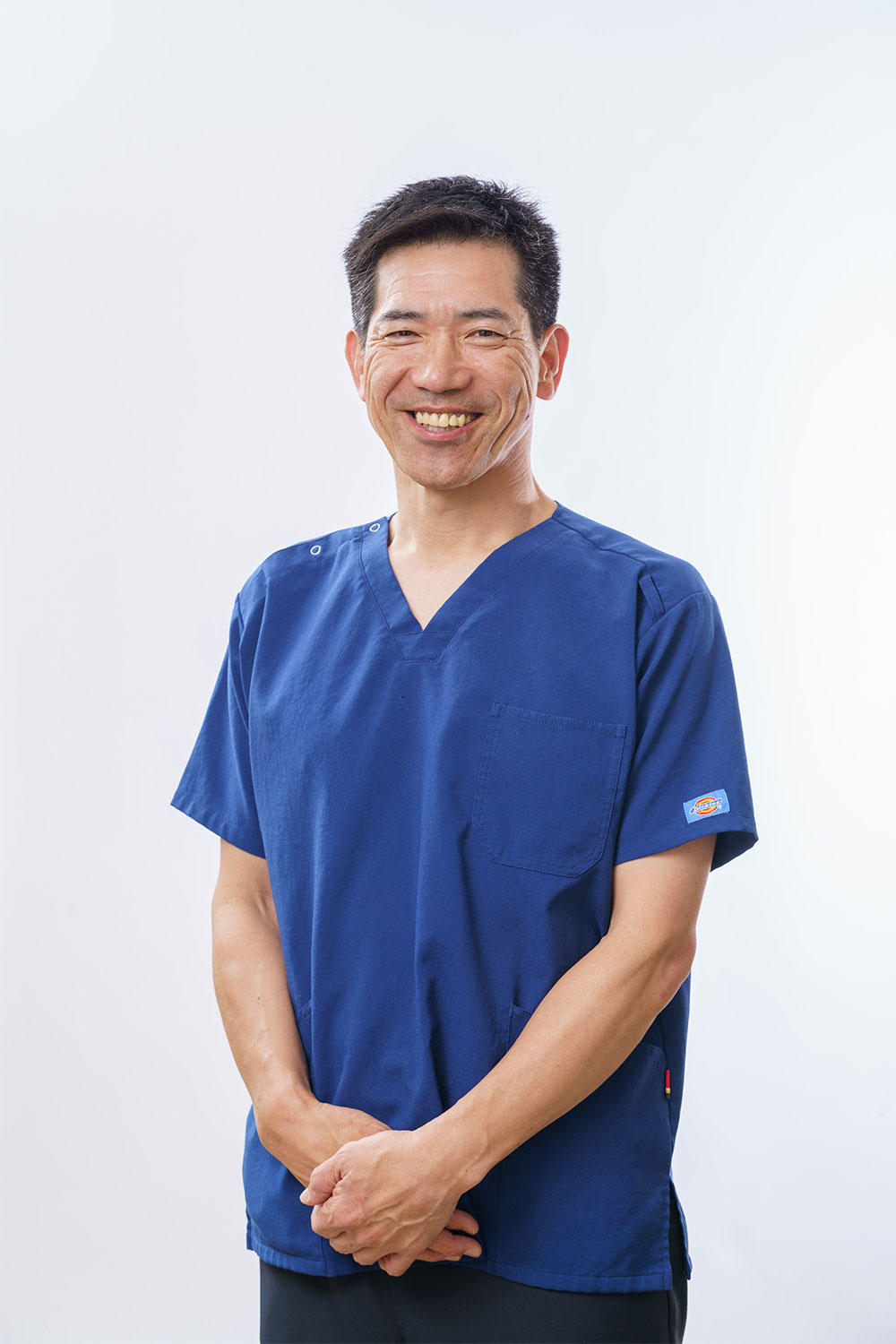 紺色のスクラブを着て正面を向いて立つ施術者