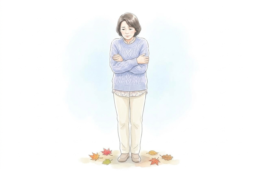 落ち葉の上で、寒さに腕を組んで体を縮こませている女性のイラスト